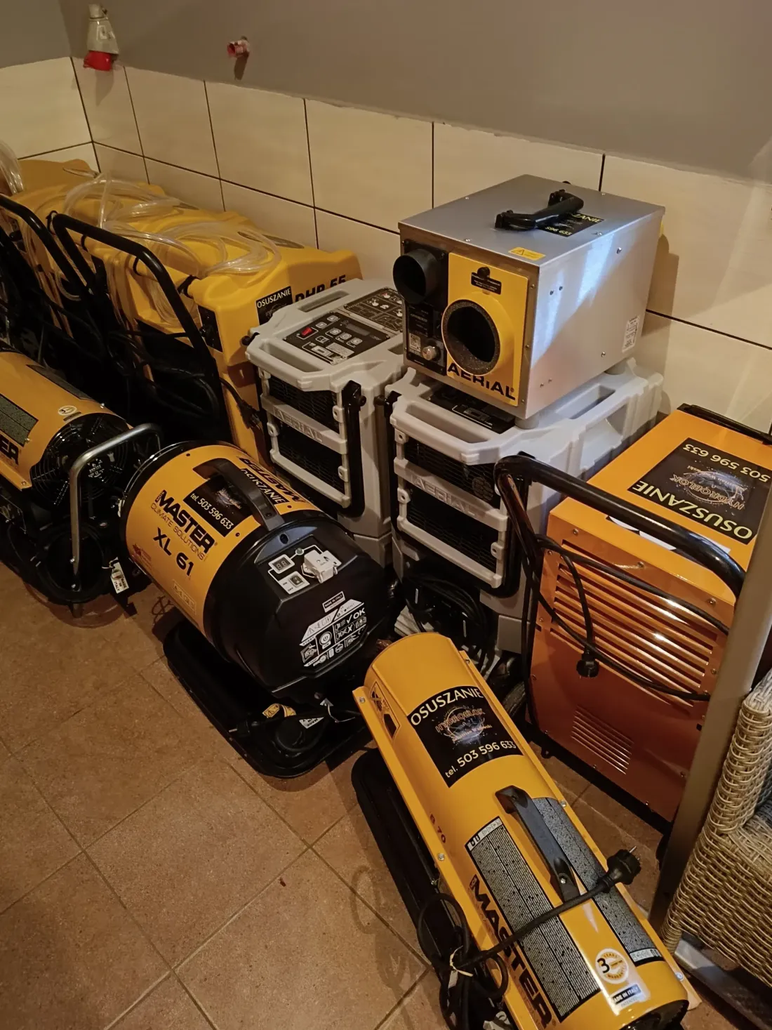 Zbliżenie na spiętrzony sprzęt do osuszania MASTER XL 61 z widocznym napisem OSUSZANIE i numerem telefonu